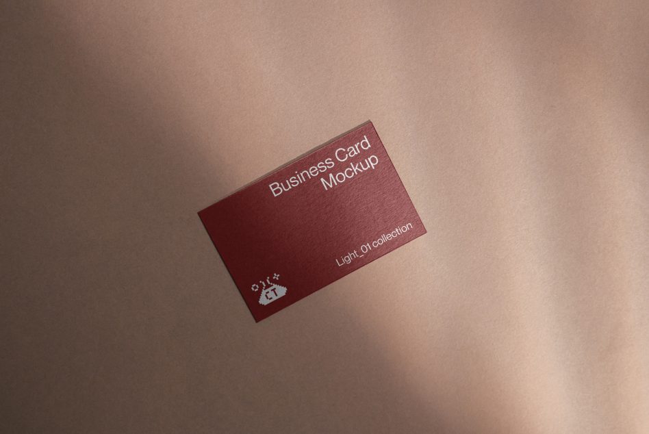 Maroon business card with white text on beige surface with soft shadow